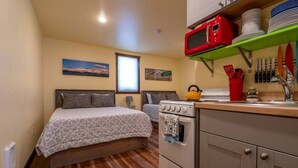 Habitación compacta con cama, kitchenette, estufa y microondas.