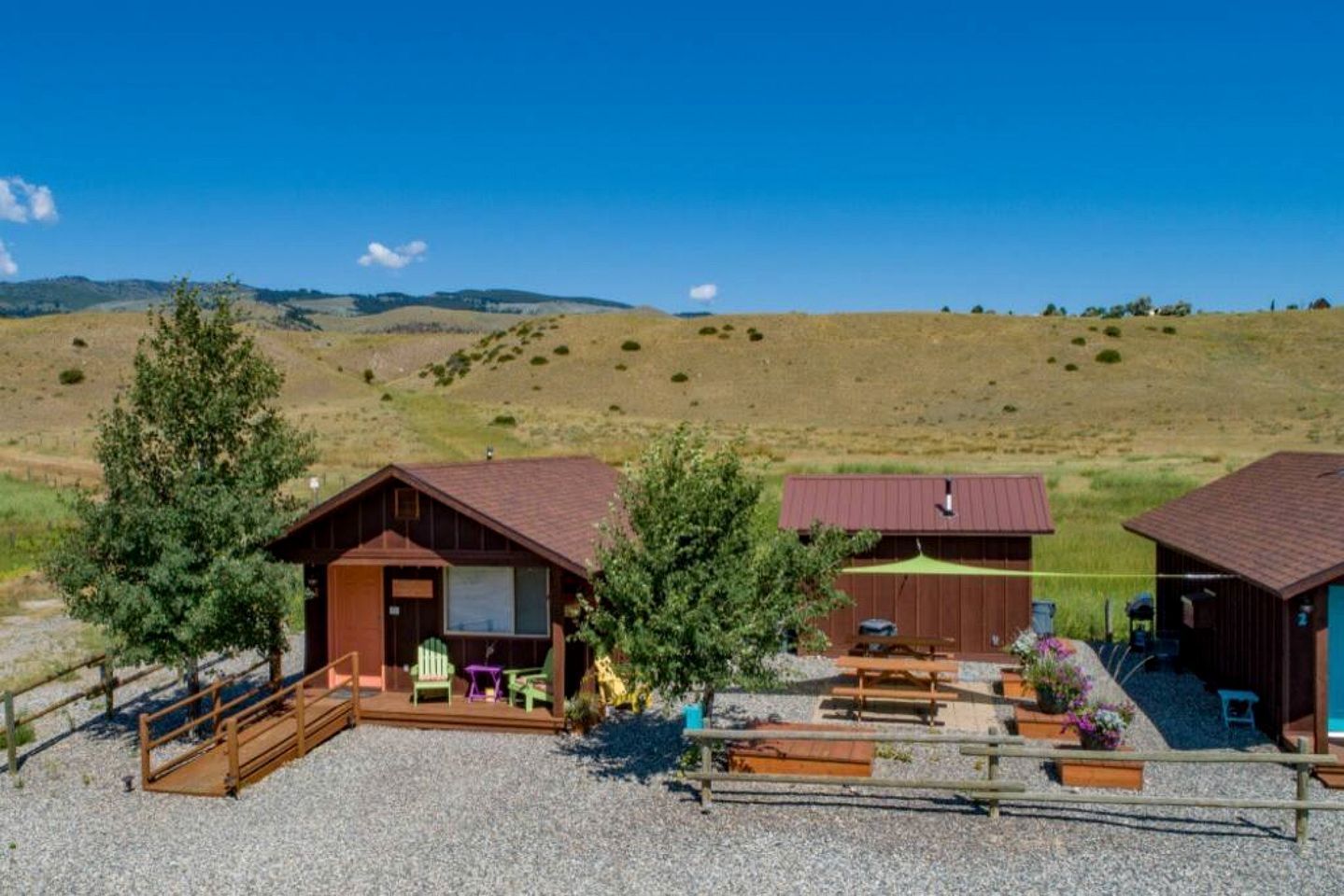 Un chalet rustique avec une allée en gravier, un espace pique-nique couvert et une vue sur des collines ondoyantes.