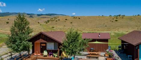 A rustic cabin with a gravel driveway, a covered picnic area, and a view of rolling hills.