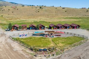 Un camping con varias cabañas, una piscina y una zona vallada con sillones de descanso.