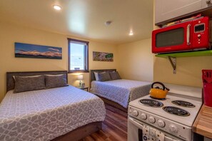 Una habitación pequeña y acogedora con dos camas, una kitchenette con estufa y microondas, y un ventanal con vistas.