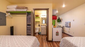 Ein Zimmer mit zwei Betten, einer kleinen Küchenzeile, einem Badezimmer und einem Flur, der zu einem weiteren Zimmer führt.