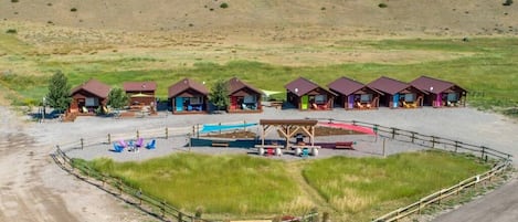A campground with multiple cabins, a swimming pool, and a fenced area with lounge chairs.