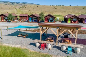 Un camping con cabañas de madera, mesas de picnic y un espacio de estar techado.