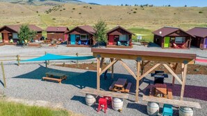 Ein Campingplatz mit Holzhütten, Picknicktischen und einer überdachten Sitzgelegenheit.