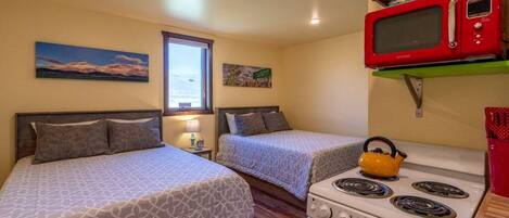 A small, cozy room with two beds, a kitchenette with a stove and microwave, and a window with a view.