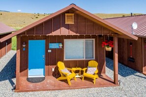 A cabin with a blue door, two yellow chairs, a small table, and a window. - Cozy Tiny Cabin with Breathtaking Emigrant Peak Views for an Amazing Escape in Montana (Emigrant)