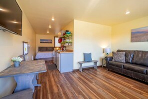 Un espacio habitable compacto con kitchenette, sofá, mesa de comedor y cama.
