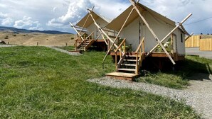A row of simple, wooden, single-story cabins with external staircases, set in a grassy field with a clear sky.