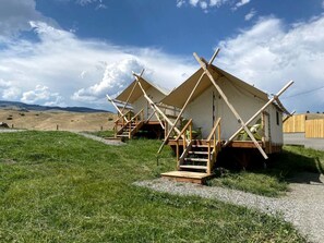 A row of simple, wooden, single-story cabins with external staircases, set in a grassy field with a clear sky.