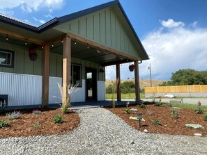 A building with a covered porch, gravel pathway, and a fenced area with plants.