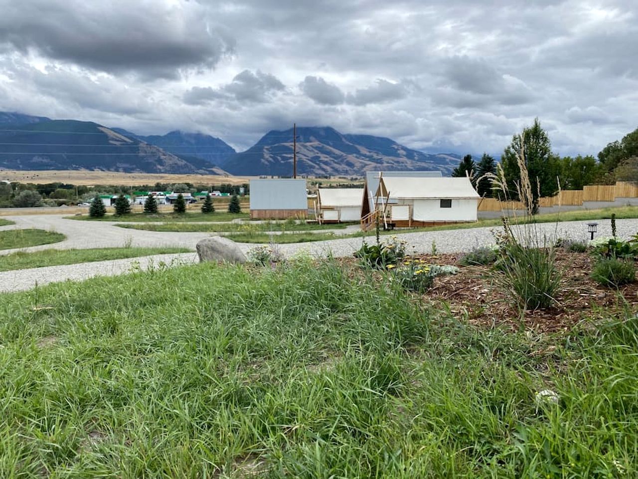 A rural landscape with a small building, a gravel path, and mountains in the background.