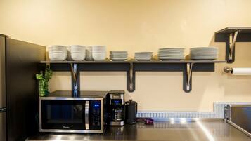 A kitchen with a microwave, coffee maker, and stacked plates on shelves.