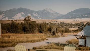 A campsite with a metal fire pit, four Adirondack chairs, and a view of mountains.