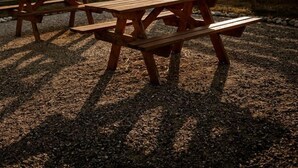 Et skyggefuldt picnicområde med træbænke og borde, omgivet af et træhegn og en stenvæg.