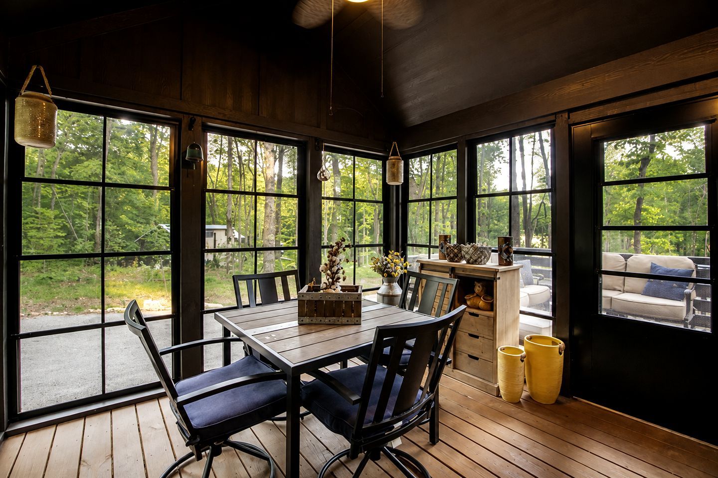Un coin repas en bois, avec une table, des chaises et une vue sur l’extérieur grâce à de grandes fenêtres.