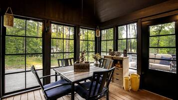 Un coin repas en bois, avec une table, des chaises et une vue sur l’extérieur grâce à de grandes fenêtres.
