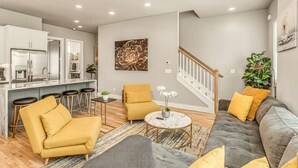 A modern living room with a sofa, armchairs, a coffee table, and a kitchen area with bar stools. - Grill Fire Pit Views Near Downtown Nashville (Nashville)