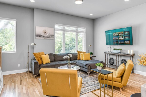 A modern living room with a sectional sofa, a yellow armchair, a coffee table, and a TV mounted on the wall. - Grill Fire Pit Views Near Downtown Nashville (Nashville)