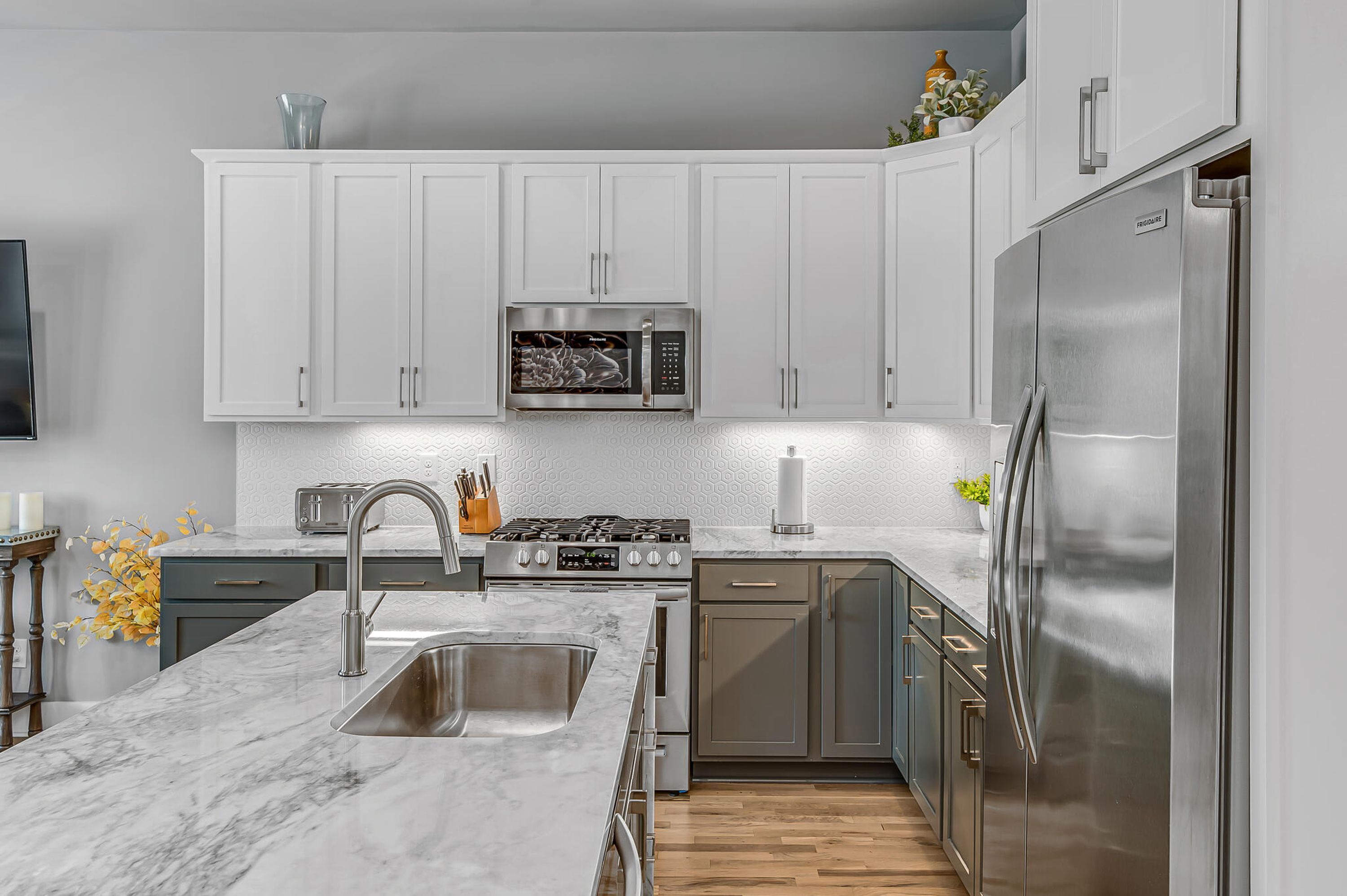 A modern kitchen with white cabinets, stainless steel appliances, and a marble countertop.