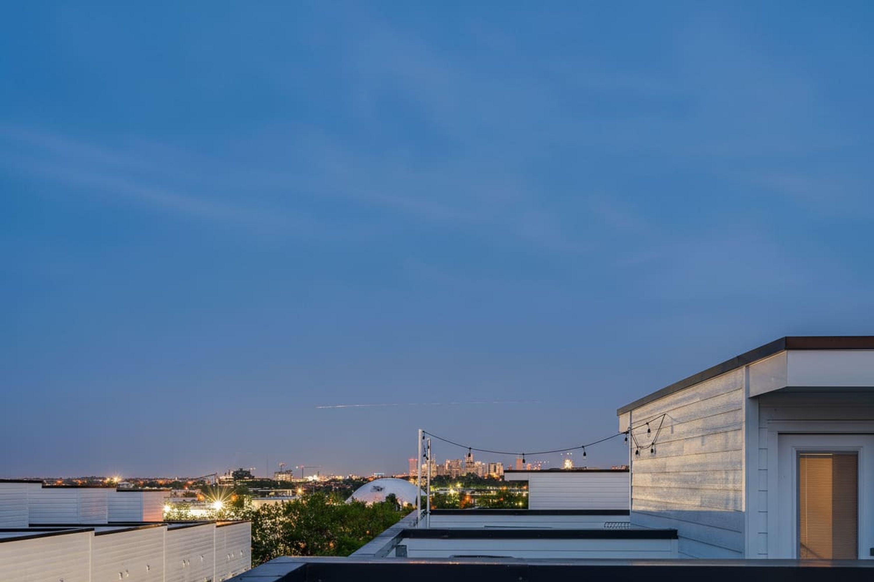 Una azotea con vistas al horizonte de una ciudad al anochecer, que incluye un edificio con forma de cúpula y luces colgantes.
