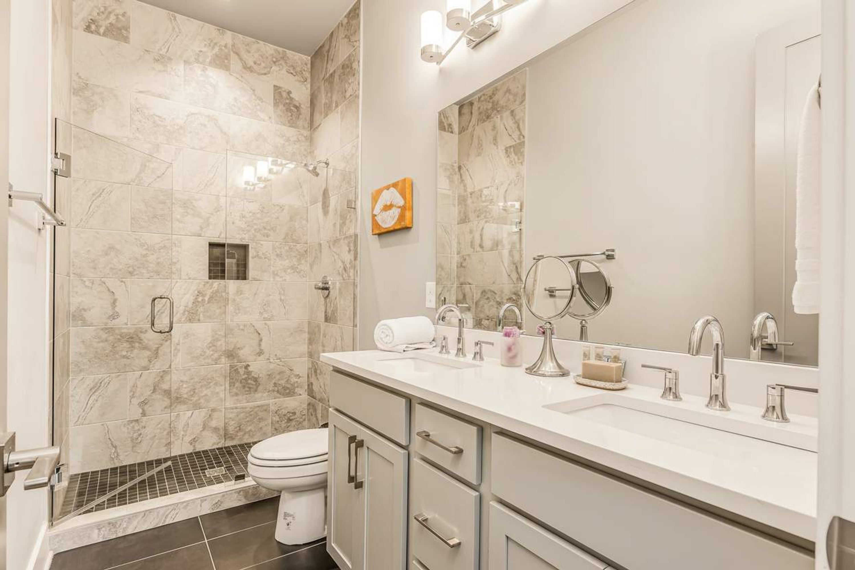 Une salle de bain moderne équipée d’une douche, de toilettes et d’un meuble-lavabo avec un grand miroir.