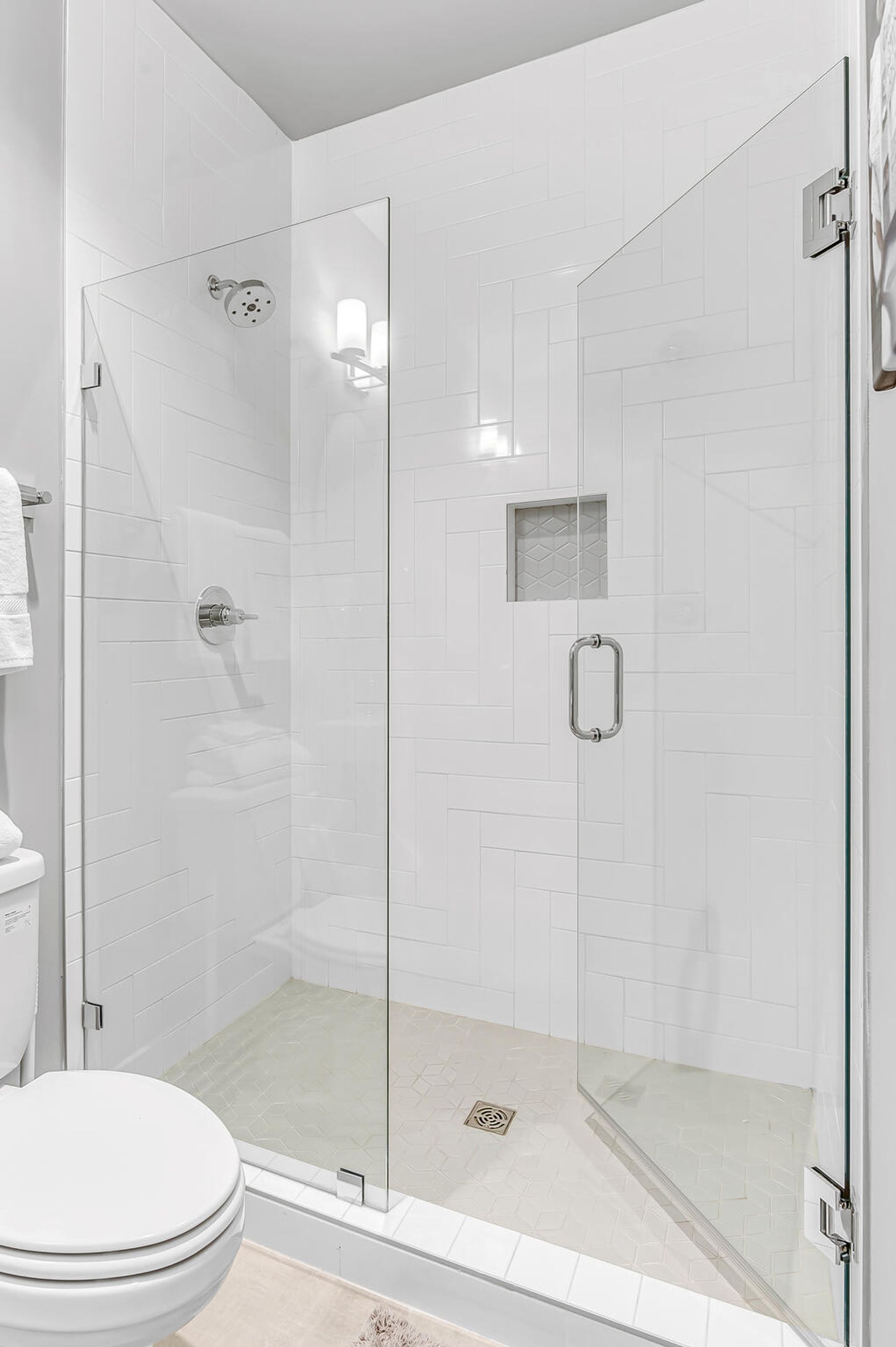 A modern bathroom with a glass-enclosed shower, white tiled walls, and a toilet.