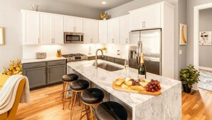 A modern kitchen with white cabinets, stainless steel appliances, a marble island, and bar stools. - Grill Fire Pit Views Near Downtown Nashville (Nashville)