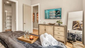 A modern bedroom with a bed, a wooden dresser, a TV, and a mirror. - Grill Fire Pit Views Near Downtown Nashville (Nashville)