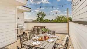 An outdoor patio with a dining table set for six, surrounded by chairs, a grill, and string lights. - Grill Fire Pit Views Near Downtown Nashville (Nashville)