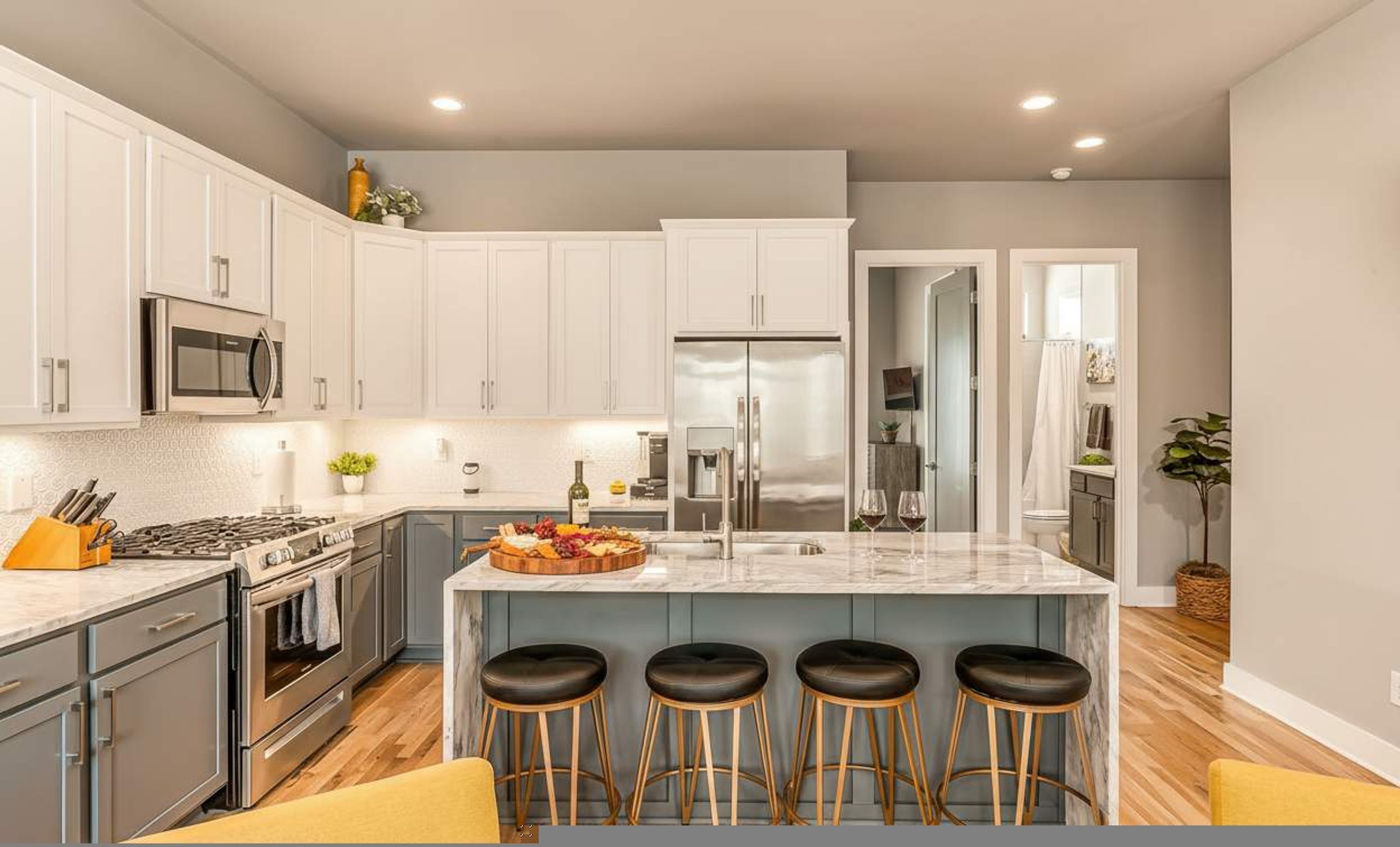 Una cocina moderna con armarios blancos, electrodomésticos de acero inoxidable, una isla de mármol con taburetes altos y suelo de madera.