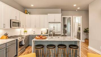 Una cocina moderna con armarios blancos, electrodomésticos de acero inoxidable, una isla de mármol con taburetes altos y suelo de madera.