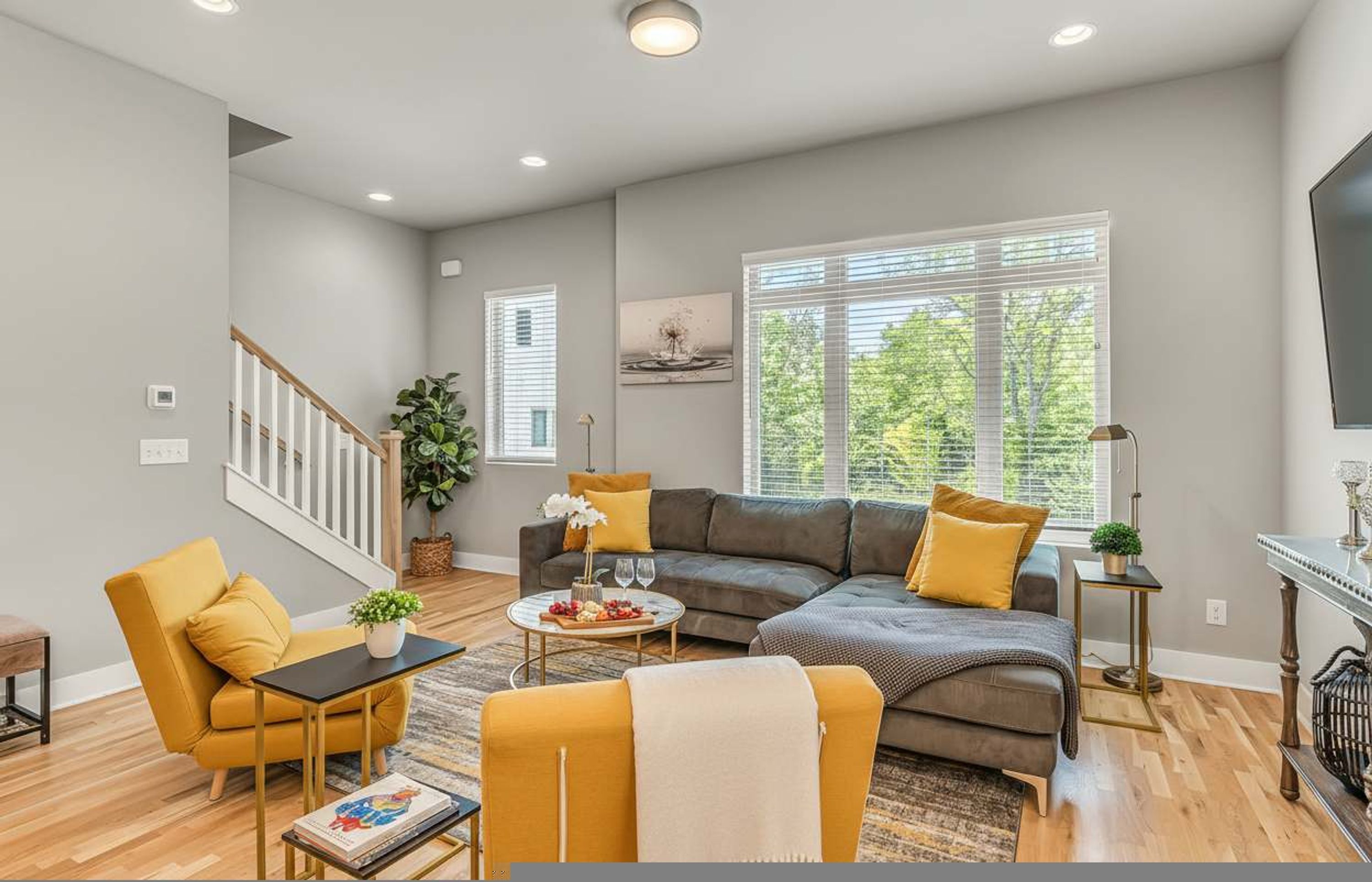 A modern living room with a sectional sofa, a yellow armchair, and a coffee table. There is a staircase with a railing leading to another level.