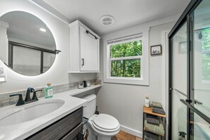 Une salle de bain moderne avec un grand miroir, des toilettes, un lavabo et une fenêtre donnant sur des arbres.
