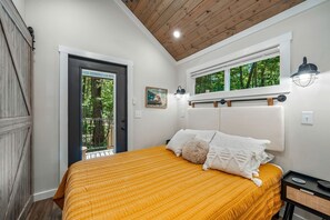 A bedroom with a bed, a window, a door, and a wall-mounted light fixture.