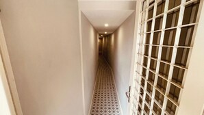A narrow hallway with patterned floor tiles, a white door with a grid pattern, and a ceiling with recessed lighting. - Torrinha's Backyard ** Porto Center (Porto)