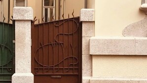 A gated entrance with a metal gate and stone pillars, leading to a building with multiple windows. - Torrinha's Backyard ** Porto Center (Porto)