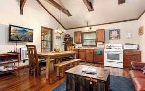 Un salón acogedor con una mesa de comedor de madera, un sofá de cuero y un televisor montado en la pared.