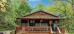 A wooden cabin with a porch, a front door, and a small deck area.
