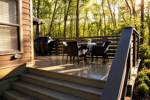 A wooden deck with outdoor furniture, a barbecue grill, and a view of a forest. - Picturesque Tiny Cottage with Cozy Indoor and Outdoor in Tennessee (Monteagle)
