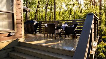 Une terrasse en bois avec des meubles d’extérieur, un barbecue et une vue sur une forêt.