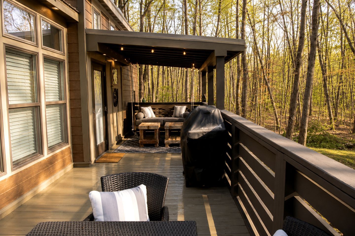 A covered outdoor seating area with a sofa and chairs, a grill, and a wooden deck.