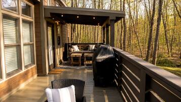 A covered outdoor seating area with a sofa and chairs, a grill, and a wooden deck.