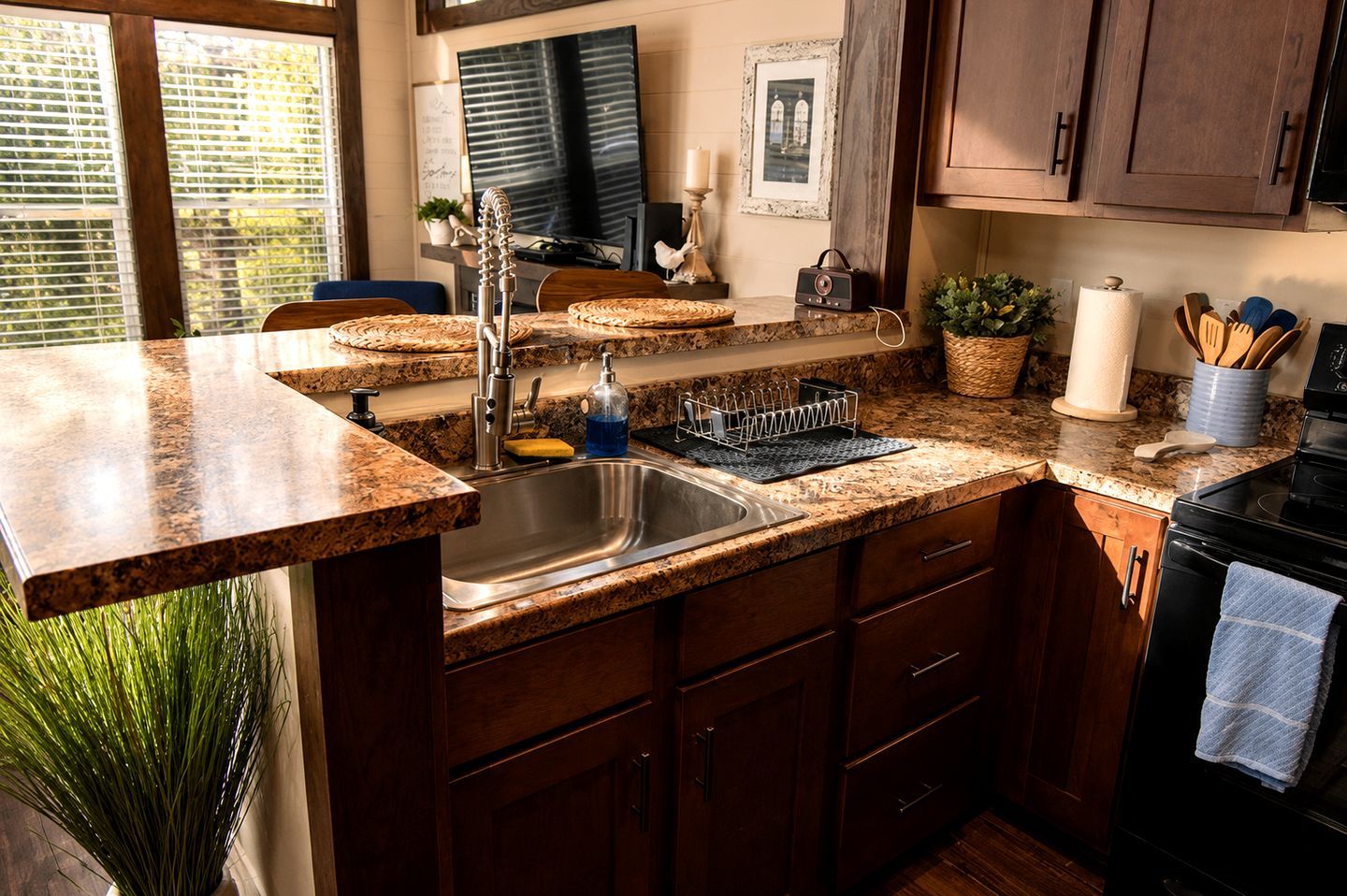 Una cocina con encimeras de granito, pileta de acero inoxidable, alacenas de madera y estufa negra.
