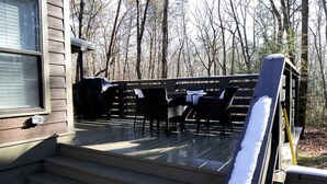 A wooden deck with outdoor furniture, steps leading to a porch, and a forested background. - Picturesque Tiny Cottage with Cozy Indoor and Outdoor in Tennessee (Monteagle)