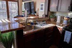 Cocina con encimeras de granito, pileta de acero inoxidable, muebles de madera, estufa negra y ventana con persianas.