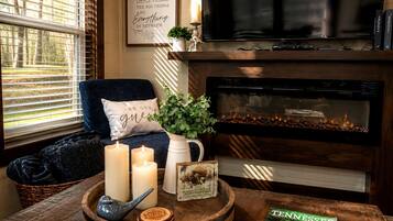 Una sala de estar acogedora con chimenea, un sillón cómodo, velas y una revista sobre una mesa de madera.
