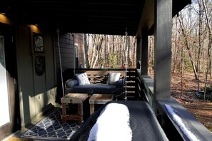 A covered outdoor seating area with a sofa, two wooden tables, and a patterned rug. - Picturesque Tiny Cottage with Cozy Indoor and Outdoor in Tennessee (Monteagle)