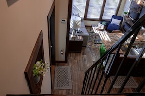 Una escalera conduce a una sala de estar con un sofá, una silla, una mesa de centro y vistas al exterior a través de amplios ventanales.
