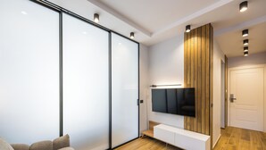 A modern living room with a sliding glass door, a flat-screen TV mounted on a wooden panel wall, a white console table, and a wooden floor. - Tribunali Trendy Accommodations by Wonderful Italy (Naples)